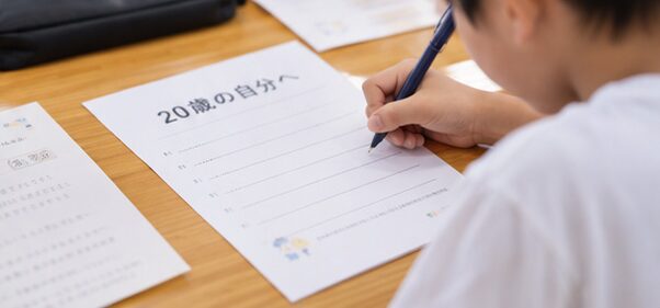 「20歳の自分へ」と書かれた用紙に手紙を書く子ども